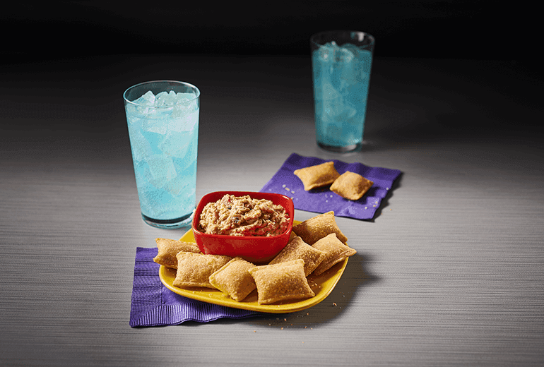 Totino's Salsa Bean Dip Recipe on a yellow plate surrounded by Totino's Pizza Rolls and accompanied by two blue sodas.