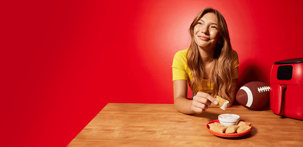 Girl eating a plate of Totino's pizza rolls with a white dip sitting at a wooden table with a football on it