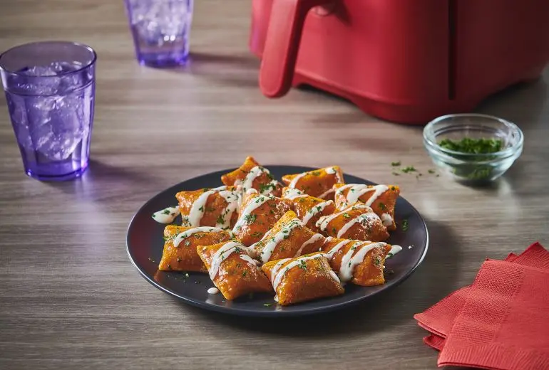 Totino's Buffalo Ranch Pizza Rolls recipe on a black plate alongside two glasses of water and an air fryer.