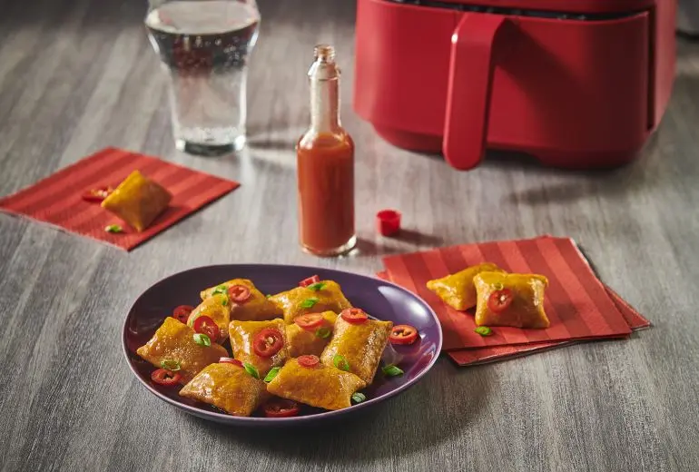 Totino's Habanero Pizza Rolls recipe on a purple plate alongside hot sauce, an air-fryer, a glass of soda, and two red napkins.
