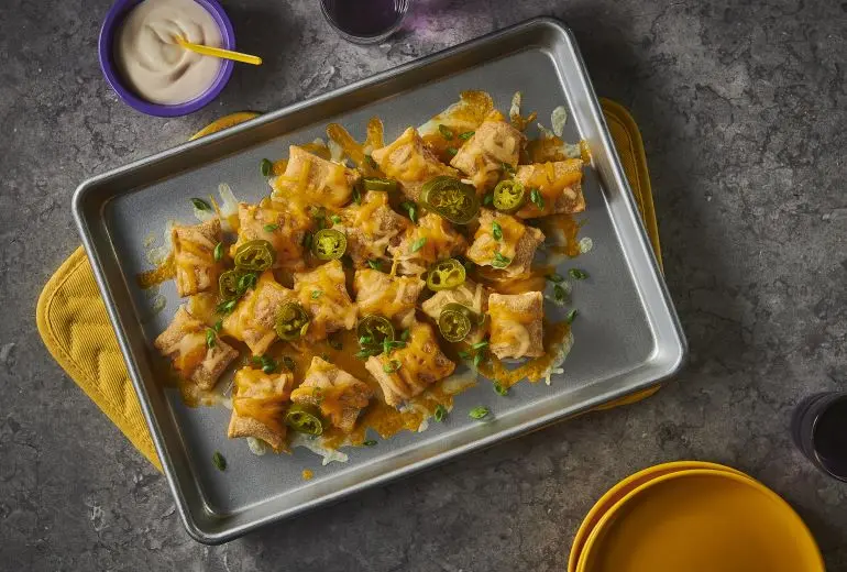 Totino's Nacho Pizza Rolls recipe on a metal baking sheet with cheese and jalapenos and a side of dip.