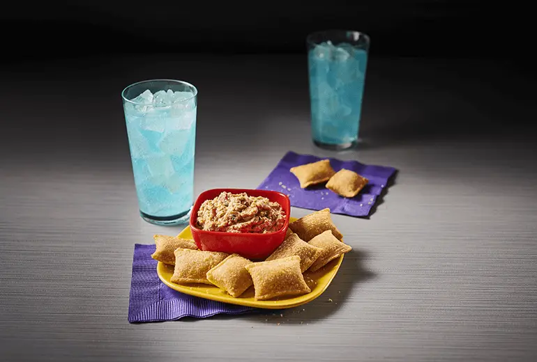 Totino's Salsa Bean Dip Recipe on a yellow plate surrounded by Totino's Pizza Rolls and accompanied by two blue sodas.