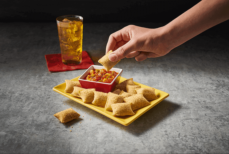 A hand dipping Totino's Pizza Rolls into the Totino's Hawaiian Pizza Dipping Sauce recipe with a glass of soda