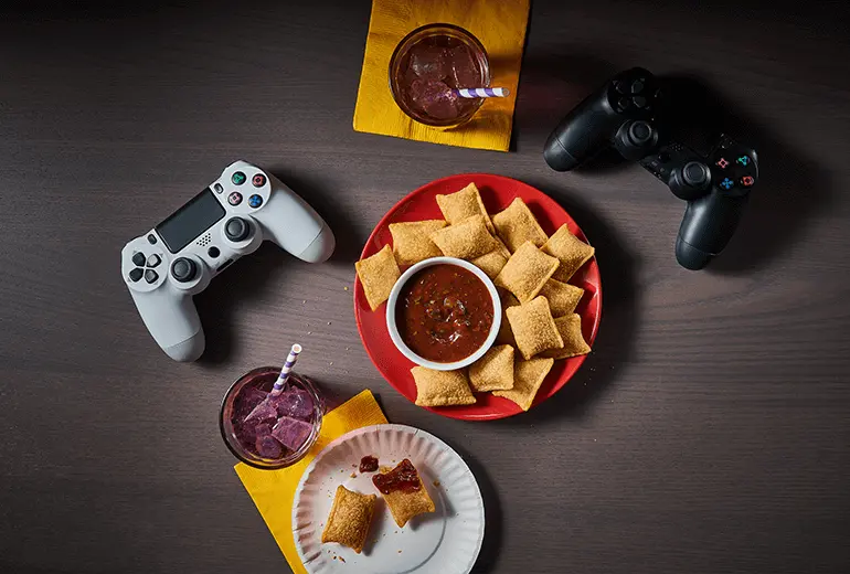 Totino's Spicy Barbecue Sauce Dip recipe on a red plate surrounded by Totino's Pizza Rolls with two game controllers and sodas on the side.